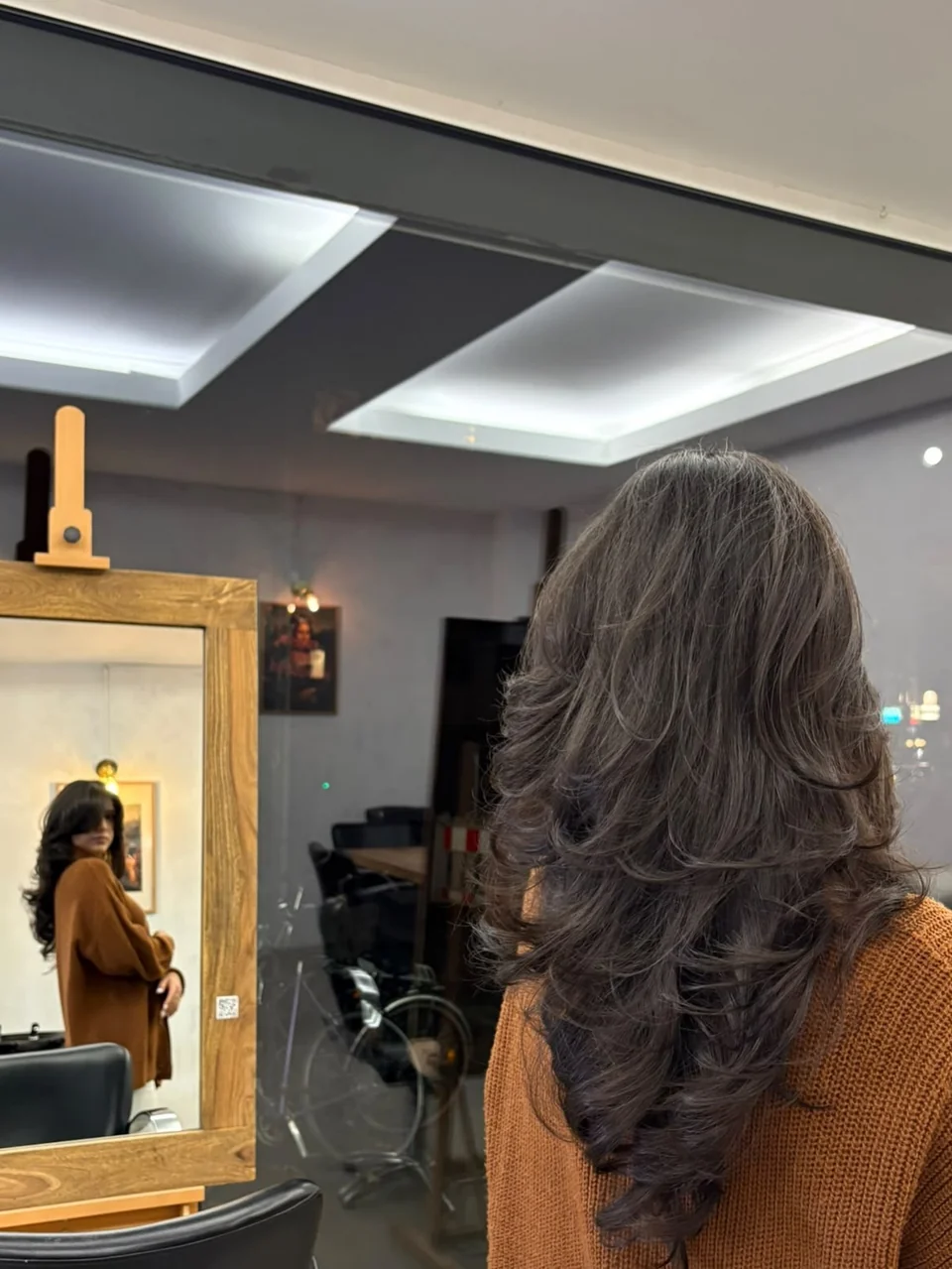 Rückansicht des langen Stufenschnitts vor einem goldenen Salonspiegel